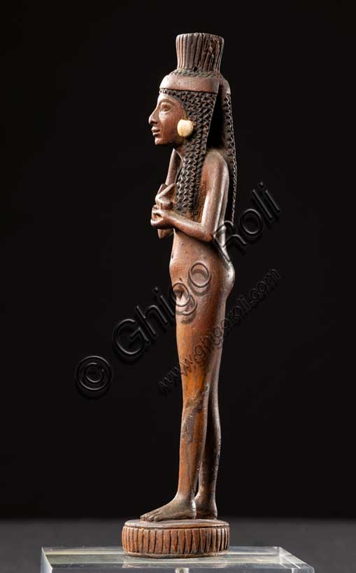 Museo Civico Archeologico di Bologna:  manico di specchio in legno e avorio; Nuovo Regno, fine XVIII - inizi XIX dinastia (1539-1190 a.C.).Inv. EG 1859.Il corpo aggraziato e sensuale di questa fanciulla serviva da manico per uno specchio di metallo, uno degli oggetti da toilette più ambiti dalle signore egiziane facoltose. Un disco in bronzo o in argento, ora scomparso, era fissato alla testa della statuetta. I lunghi riccioli, trattenuti da una fascia che si annoda dietro la testa, e i grandi orecchini in avorio attirano inizialmente sul volto l’attenzione di chi guarda, ma il gesto noncurante con il quale la fanciulla sposta una ciocca di capelli dietro la spalla destra, stringendo al petto un uccellino dalle ali dischiuse, mentre avanza in modo quasi impercettibile la gamba sinistra e divarica un poco i piedi, induce a percorrere l’intera nudità del corpo, caratterizzato da delicata prosperosità e vitale tensione. Era forse così, eternamente giovane, che la proprietaria dello specchio avrebbe desiderato scoprirsi ogni mattina, nell’utilizzarlo per la cura e la cosmesi del proprio corpo.