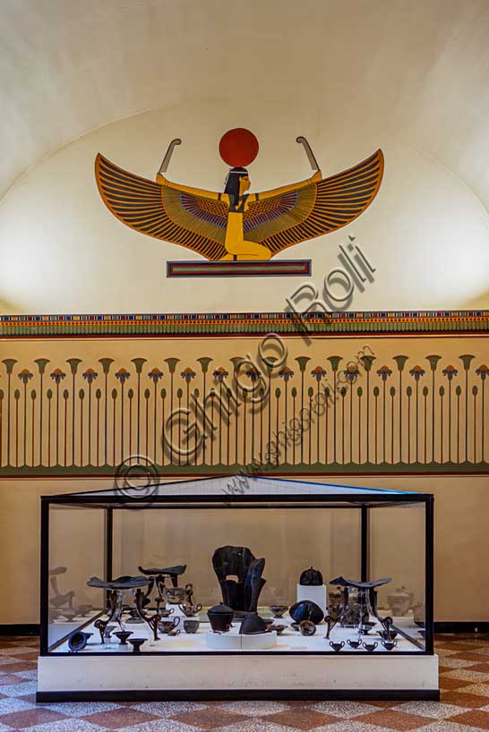 Museo Civico Archeologico di Bologna, sala III: l’allestimento del corredo della tomba 85 dalla necropoli Lippi di Verucchio, uno dei centri Etruschi di maggiore importanza della regione.Tra i materiali di corredo (deposti assieme alle ceneri di un ricco aristocratico) spicca l'imponente trono in legno, decorato ad intaglio, databile al VII secolo a.C., con poggiapiedi. E' il segno più evidente che il defunto avesse rango altissimo.Oltre al trono si segnalano, sempre appartenenti allo stesso corredo, i tre tavolini che ospitavano il vasellame in ceramica contenente le offerte di cibo per il defunto. Tra i cibi è ancora possibile riconoscere uva, nocciole, carne e pesce. A lato del trono vi è un grande elmo in bronzo e vimini, mentre una fibula in bronzo rivestita di preziosa ambra apparteneva all'ornanento personale del defunto.