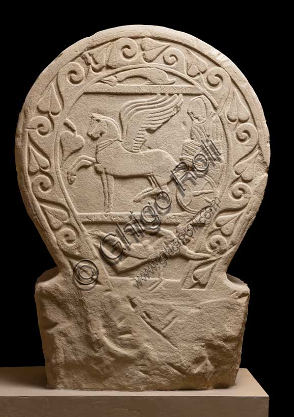 Museo Civico Archeologico di Bologna: stele funeraria etrusca decorata su entrambi i lati e nello spessore, lato A. Proveniente dal sepolcreto dei Giardini Margherita.inv. DUCATI_012Una donna dalla stirpe eroica. La stele Ducati 12, o di Rakvi Satlnei, è stata ritrovata presso la necropoli dei Giardini Margherita, collocata a ovest della città antica, ed è datata attorno al 400 a.C.  Questo lato è occupato dal tema del passaggio di status, cioè la morte, reso attraverso l’espediente del viaggio su carro della defunta. Sotto è raffigurato un personaggio maschile nudo che si getta su una spada, riconosciuto come l’eroe omerico Aiace Telamonio. Sulla stele è presente un’iscrizione che, in alcuni punti, è di difficile lettura. Si riesce a distinguere il prenome, Rakvi, e il gentilizio, Satlnei, della donna. È importante sottolineare che si tratterebbe dell’unico caso attestato in tutta Bologna. La seconda parte è molto dibattuta dalla critica ma sembra collegarsi alla raffigurazione di Aiace Telamonio. Infatti, le lettere leggibili sembrano comporre le parole aivas telmuns. Attraverso le informazioni grammaticali in nostro possesso, si è pensato che venga evocato un rapporto genealogico della defunta con l’eroe.