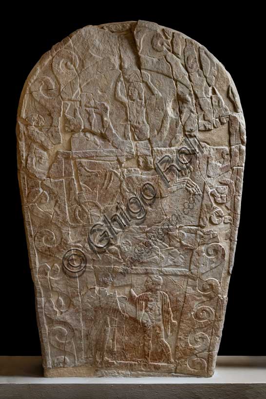 Museo Civico Archeologico di Bologna: Stele funeraria etrusca decorata su quattro registri. Questa stele di dimensioni monumentali, è decorata a bassorilievo su entrambi i lati.ll tema del passaggio del defunto dalla vita alla morte è descritto mediante due scene diverse, in cui compare sempre un demone alato, che, su un lato, “rapisce” il defunto portandolo per mano nell’Aldilà, sull’altro lo guida verso l'oltretomba su una biga trainata da cavalli alati.Questa seconda raffigurazione si inserisce in una delle tre fasce in cui è suddiviso uno dei lati della stele; nelle altre due fasce vi sono, in basso, una rappresentazione di giochi funebri, con un cavaliere etrusco armato che affronta un guerriero nudo con spada e scudo; in alto la lotta tra un serpente ed un ippocampo, animali fantastici che alludono al mondo ultraterreno.Provenienza: Bologna, necropoli della Certosa, tomba 89.Numero di inventario: Ducati 169