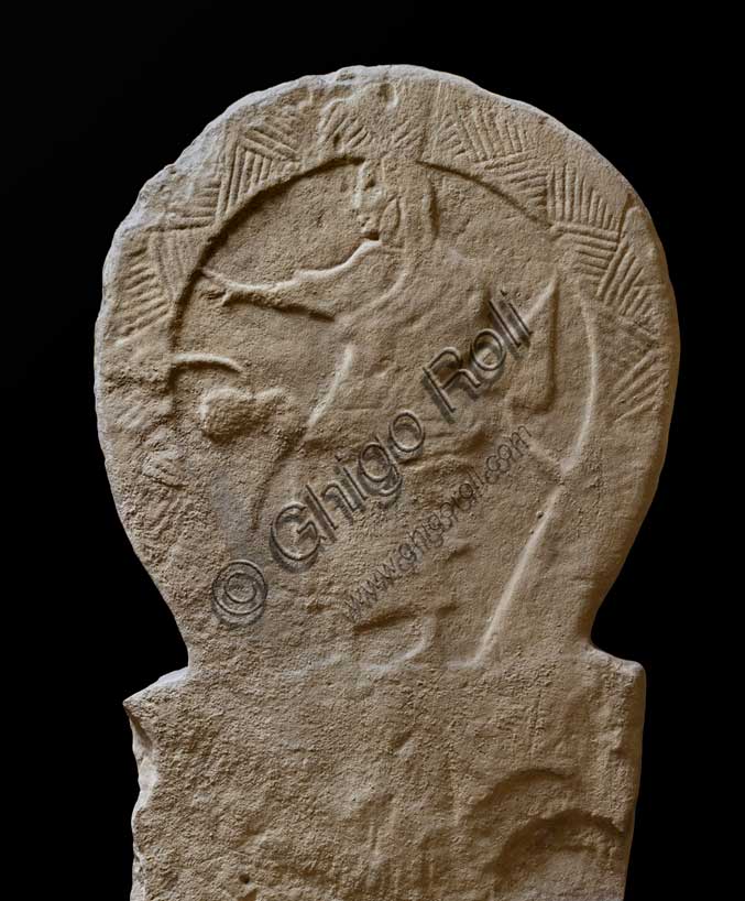 Museo Civico Archeologico di Bologna: Stele funeraria etrusca decorata su entrambi i lati e nello spessore, lato B. Proveniente dal sepolcreto dei Giardini Margherita.inv. DUCATI_012Una donna dalla stirpe eroica. La stele Ducati 12, o di Rakvi Satlnei, è stata ritrovata presso la necropoli dei Giardini Margherita, collocata a ovest della città antica, ed è datata attorno al 400 a.C. Un lato della stele mostra la tipica rappresentazione della donna nobile sposata che solleva una mano verso una foglia di edera, la quale esce dalla cornice decorata con triangoli alterni. Questa è una pianta legata al culto del dio Dioniso, l’etrusco Fufluns. Si sottolinea così lo status sociale della defunta e la sua adesione ai culti dionisiaci. 