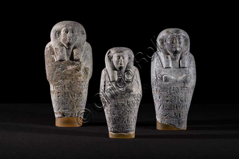 Museo Civico Archeologico di Bologna: tre statuette ushabti di Petamenophis.Inventario EG 2168 - 2169 - 2170. Gli ushabti sono statuine funerarie, dall’aspetto mummiforme (con il corpo a forma di mummia) che tengono nelle mani, incrociate al petto, attrezzi agricoli, quali zeppe, marre e un sacchetto per le sementi. Realizzati in diversi materiali (legno, pietra, terracotta, faïence), erano parte del corredo funerario, cioè l’insieme di oggetti posti nella tomba al fianco del defunto per accompagnarlo nel suo viaggio nell’Aldilà. L’uso di queste particolari statuette funerarie risale al Medio Regno (XIX-XVIII secolo a.C.), quando iniziò a esserne introdotto un esemplare per tomba, nelle sepolture dei privati. Nel corso del tempo il loro numero tuttavia crebbe fino a raggiungere le centinaia per singola sepoltura, tanto regale quanto privata. La maggior parte di queste statuette reca iscritta la formula VI del Libro dei Morti, con cui l’Ushabti, che secondo l’etimologia più accettata significa “colui che risponde”, era chiamato a effettuare lavori agricoli nei campi di Osiride nell’Aldilà. Erano considerati perlopiù come «doppi», o servitori del defunto, con la funzione di sostituirsi a lui nelle mansioni lavorative dell’Aldilà. 