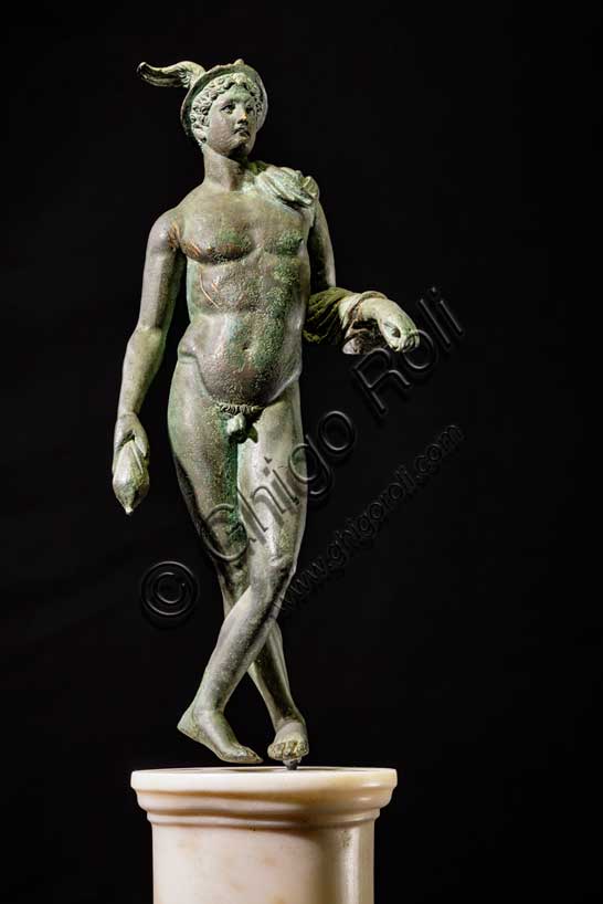 Museo Civico Archeologico di Bologna:“Mercurio”, bronzetto da Castelvetro, podere Selmi. I sec. a.C.- I sec. d. C. Mercurio è il dio romano identificato con l'Ermes greco, l'astuto messaggero degli dei, figlio di Zeus, incaricato di fare da intermediario tra il mondo degli uomini e quello degli dei. E' la divinità che protegge i commercianti e i viaggiatori. I suoi attributi sono il caduceo, la verga simbolica degli araldi, il petaso, il cappello a larga tesa con le ali, i sandali alati e una borsa, simbolo del guadagno ricavato dalle attività mercantili.La statuetta raffigura il dio in posizione di riposo, con le gambe incrociate, appoggiato col braccio sinistro ad un sostegno, ora scomparso. Indossa il petaso alato, e porta un corto mantello avvolto alla spalla e al braccio sinistro; con la mano destra stringe la borsa, nella sinistra aveva probabilmente il caduceo. E' un bronzetto di buona fattura attribuibile a una officina romana della prima età imperiale.Inv. ROM_1522