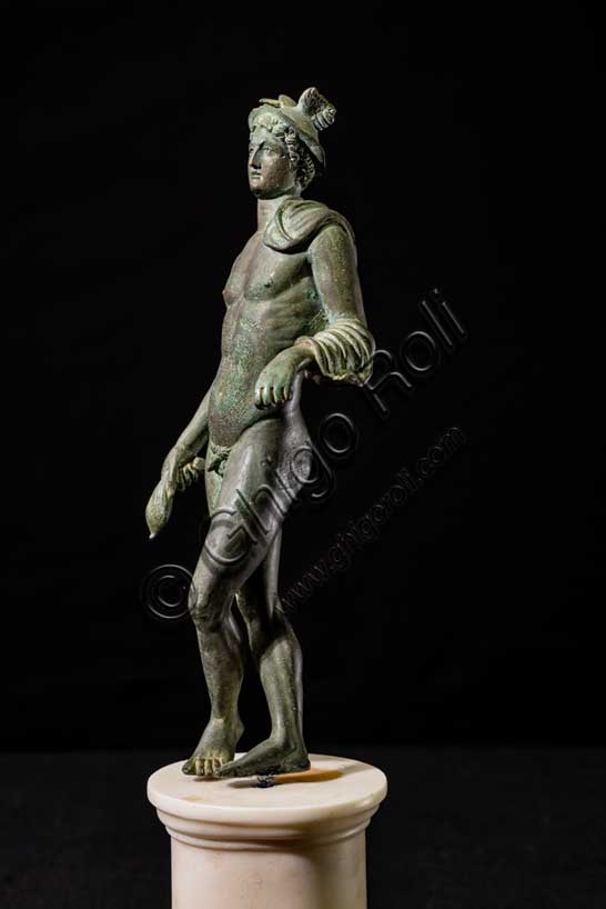 Museo Civico Archeologico di Bologna:“Mercurio”, bronzetto da Castelvetro, podere Selmi. I sec. a.C.- I sec. d. C. Mercurio è il dio romano identificato con l'Ermes greco, l'astuto messaggero degli dei, figlio di Zeus, incaricato di fare da intermediario tra il mondo degli uomini e quello degli dei. E' la divinità che protegge i commercianti e i viaggiatori. I suoi attributi sono il caduceo, la verga simbolica degli araldi, il petaso, il cappello a larga tesa con le ali, i sandali alati e una borsa, simbolo del guadagno ricavato dalle attività mercantili.La statuetta raffigura il dio in posizione di riposo, con le gambe incrociate, appoggiato col braccio sinistro ad un sostegno, ora scomparso. Indossa il petaso alato, e porta un corto mantello avvolto alla spalla e al braccio sinistro; con la mano destra stringe la borsa, nella sinistra aveva probabilmente il caduceo. E' un bronzetto di buona fattura attribuibile a una officina romana della prima età imperiale.Inv. ROM_1522