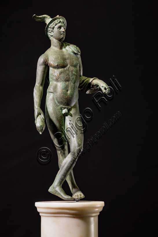 Museo Civico Archeologico di Bologna:“Mercurio”, bronzetto da Castelvetro, podere Selmi. I sec. a.C.- I sec. d. C. Mercurio è il dio romano identificato con l'Ermes greco, l'astuto messaggero degli dei, figlio di Zeus, incaricato di fare da intermediario tra il mondo degli uomini e quello degli dei. E' la divinità che protegge i commercianti e i viaggiatori. I suoi attributi sono il caduceo, la verga simbolica degli araldi, il petaso, il cappello a larga tesa con le ali, i sandali alati e una borsa, simbolo del guadagno ricavato dalle attività mercantili.La statuetta raffigura il dio in posizione di riposo, con le gambe incrociate, appoggiato col braccio sinistro ad un sostegno, ora scomparso. Indossa il petaso alato, e porta un corto mantello avvolto alla spalla e al braccio sinistro; con la mano destra stringe la borsa, nella sinistra aveva probabilmente il caduceo. E' un bronzetto di buona fattura attribuibile a una officina romana della prima età imperiale.Inv. ROM_1522