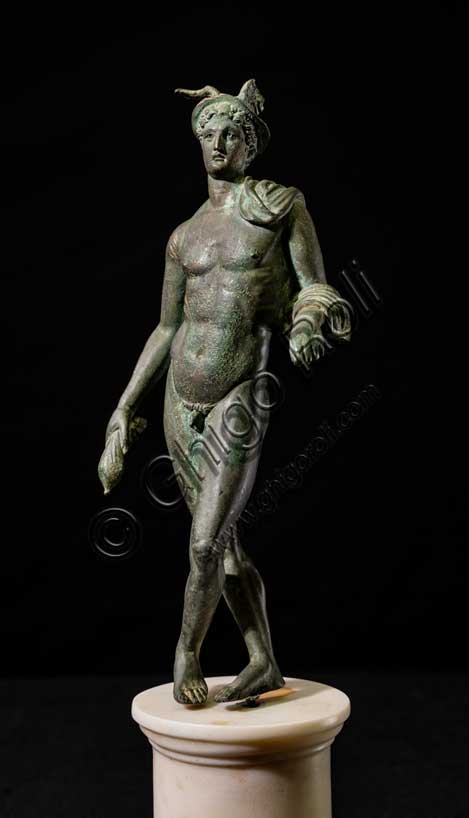 Museo Civico Archeologico di Bologna:“Mercurio”, bronzetto da Castelvetro, podere Selmi. I sec. a.C.- I sec. d. C. Mercurio è il dio romano identificato con l'Ermes greco, l'astuto messaggero degli dei, figlio di Zeus, incaricato di fare da intermediario tra il mondo degli uomini e quello degli dei. E' la divinità che protegge i commercianti e i viaggiatori. I suoi attributi sono il caduceo, la verga simbolica degli araldi, il petaso, il cappello a larga tesa con le ali, i sandali alati e una borsa, simbolo del guadagno ricavato dalle attività mercantili.La statuetta raffigura il dio in posizione di riposo, con le gambe incrociate, appoggiato col braccio sinistro ad un sostegno, ora scomparso. Indossa il petaso alato, e porta un corto mantello avvolto alla spalla e al braccio sinistro; con la mano destra stringe la borsa, nella sinistra aveva probabilmente il caduceo. E' un bronzetto di buona fattura attribuibile a una officina romana della prima età imperiale.Inv. ROM_1522
