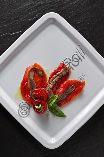 Un piatto con alici (acciughe)  e peperoni guarniti da basilico. 