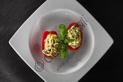   A dish of filled tomatoes covered with mayonnaise and basil leaves. 