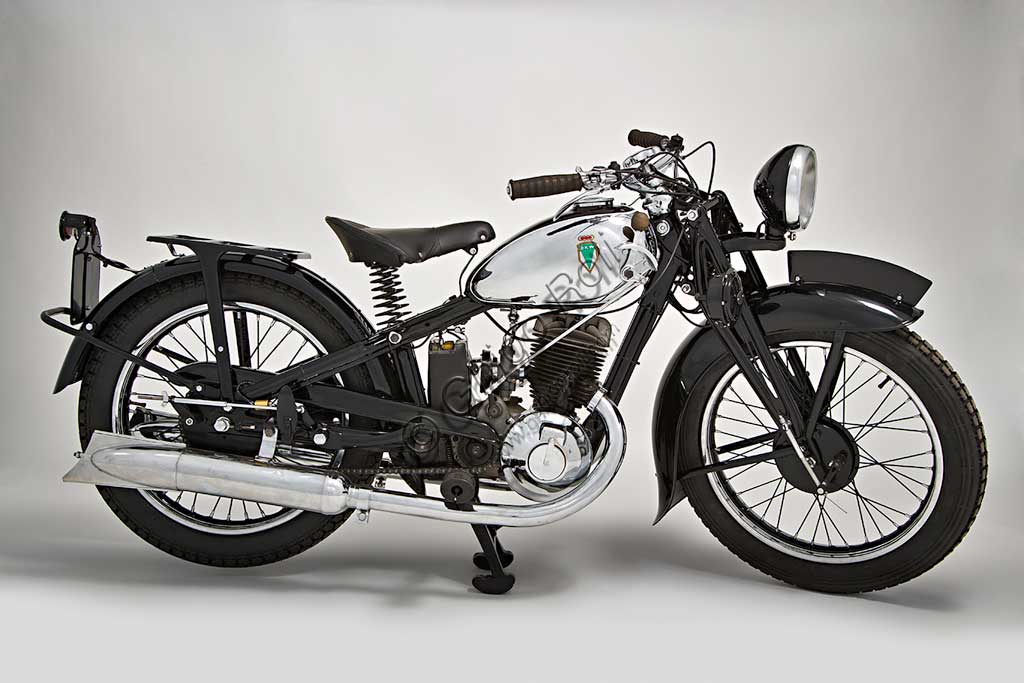 Moto d'epoca DKW UB 350 SportMarca: DKWmodello: UB 350Sportnazione: Germania - Zschopauanno: 1936condizioni: restauratacilindrata: 350motore: due tempi monocilindrico a lavaggio piattocambio: a tre rapportiLa DKW viene fondata  dall'ingegnere danese Jorge Skafte Rasmussen come fabbrica di automobili.  Nel 1919, su progetto di Hugo Ruppe, fabbrica un motore da applicare alle biciclette che, giocando sulle iniziali dell'azienda, viene battezzato  Das Kleine Wunder,  "La Piccola Meraviglia". Inizia così l'ascesa di quella marca che con decine di modelli, metterà in moto la Germania degli anni '30 e, nel 1938 raggiungerà, prima casa motociclistica al mondo, la cifra di un milione di esemplari prodotti.Questa 350, monta un motore a due tempi (come quasi tutti i modelli della casa), ma con aspirazione a lavaggio piatto, due luci di aspirazione, doppio travaso, pistone in alluminio .