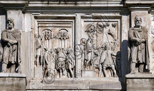 Roma, Foro Romano, Arco di Costantino: particolare dei pannelli di Marco Aurelio ( II secolo d.C.) sul lato Sud (attico).  Nel riquadro a sinistra "Rex Datus", (presentazione all'imperatore di un capo barbaro sottomesso): Marco Aurelio, accompagnato da Pompeiano, presenta al gruppo dei barbari il nuovo re tributario a lui sottomesso (Furzio?); Pompeiano è dietro di lui e sullo sfondo si vedono un edificio da accampamento e, dietro ai barbari, aquiliferi con insegne."; in quello a destra "Captivi", (prigionieri condotti all'imperatore): Marco Aurelio e Pompeiano, su un basso tribunale alla presenza di soldati con vessilli, condannano un principe barbaro (dai capelli folti e corvini), che viene spinto verso di loro con le mani legate sulla schiena; sullo sfondo è rappresentato un albero. II secolo d.C.