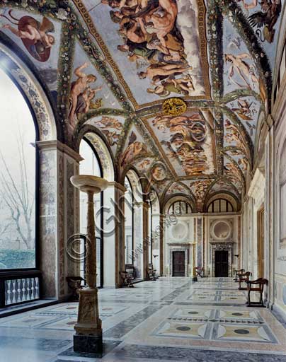 Rome, Villa Farnesina: view of the Loggia of Cupid and Psyche.The Loggia takes its name from the decoration frescoed on the vault by Raphael and his workshop in 1517-18. The frescos represent episodes from the fable of Psyche, narrated in Apuleiu’s Golden Ass, which had already been used in the fifteenth century for nuptial imagery.To give the space a festive and theatrical feel to it, Raphael also transformed the vault of the Loggia into a pergola, adorned with magnificent hanging festoons, as though the greenery of the gardens had invaded the Villa itself. In the centre he designed two fictive tapestries which depict the concluding scenes: the splendid Council of the Gods, where the unjustly persecuted girl is finally received by the gods with divine complacence, and the Marriage of Cupid and Psyche, the symbolic culmination of the entire cycle.However, although the general layout of the cycle and planning of the individual scenes and figures are attributed to the intuitive genius of Raphael (proven by a number of autographic sketches), the actual completion of the designs into frescos was carried out by his numerous workshop assistants, including Giovanni Francesco Penni, Giulio Romano and Giovanni da Udine. The latter, in particular, was the creator of the exuberant triumphal festoons.