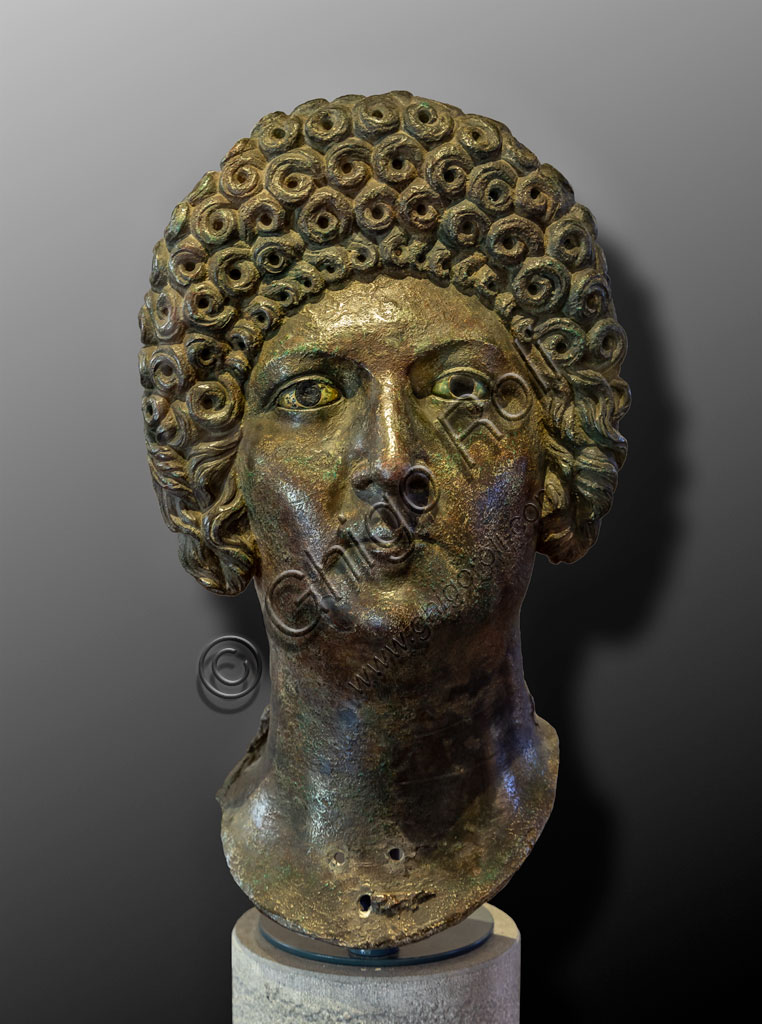 Brescia, "Santa Giulia, Museum of the City" (Unesco site since 2011):  portrait of a woman belonging to the Flavi family, bronze, lost wax casting, second half of the first century AD. The rich curly hair, often obtained with wigs, is typical of the women of the Flavi family. She could be Domizia Longina, wife of the Emperor Domitian, or Giulia, daughter of Emperor Titus.It is one of the six Roman busts found in the ancient Capitolium in 1826.