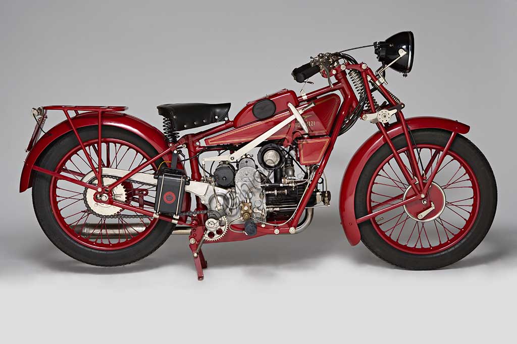 Moto d'epoca Guzzi Sport 14.Marca: Moto Guzzimodello: Sport 14nazione: Italia - Mandello Larioanno: 1929condizioni: restauratacilindrata: 498,4 cc (Alesaggio e corsa 88 x 82)motore: quattro tempi monocilindrico orizzontalecambio: in blocco a tre rapportiLa Sport 14, ultima Guzzi con serbatoio "sottocanna", si colloca come modello di transizione tra la prima Tipo Normale e i modelli di grande successo degli anni trenta. Nonostante il nome Sport, nasce come modello prevalentemente votato al turismo e si rivolge a quel pubblico ormai affezionato alla casa, che cerca moto robuste e affidabili da usare ogni giorno e anche nei viaggi più impegnativi. Una rapida occhiata ai comandi è sufficiente per capire cosa significasse guidare le moto degli anni '20: al manubrio troviamo le tre manette di gas, aria e anticipo, le tre leve di frizione, alzavalvole e freno anteriore, il pomello del frenasterzo;  al lato del serbatoio la leva del cambio, poi i pedali del freno posteriore, il rubinetto dell'olio, il rubinetto della benzina e il cicchetto, oltre naturalmente a tutti i comandi elettrici....