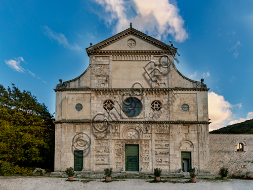 Spoleto, Chiesa di San Pietro: la facciata, caratterizzata da rilievi romanici (XII secolo). E' divisa in tre zone: la superiore è sormontata da un timpano con la statua di San Pietro. Lo spazio che era forse destinato ad accogliere un mosaico è fiancheggiato da riquadri con rilievi di S. Pietro, S. Andrea e due tori. La parte mediana è caratterizzata da tre oculi. Il centrale è inquadrato da da una decorazione cosmatesca e circondato da simboli degli Evangelisti. Nella parte inferiore si aprono tre portali fiancheggiati da animali. I portali laterali sono sormontati da rilievi. in quello  a destra è un santo vescovo, in quello a sinistra Sn Michele che abbatte il drago.