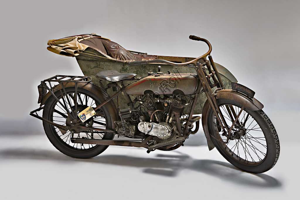 Moto d'epoca Harley-Davidson T - SideMarca: Harley-Davidsonmodello: T Sidenazione: U.S.A. - Milwaukeeanno: 1917condizioni: conservatacilindrata: 1000 (alesaggio e corsa 84,1 x 88,9)motore: bicilindrico a V di 45°cambio: a tre rapportiFondata nel 1903 la H-D ha accompagnato tutta la storia degli Stati Uniti fino ad oggi, dalle prime moto militari usate nelle schermaglie di confine contro Pancho Villa, alle grandi forniture per l'esercito che nel 1917 era entrato in guerra sul fronte europeo, dai mezzi da lavoro (i "tricicli" dei lattai e dei postini americani) alle grandi bicilindriche della polizia.. Già nel '20 era il primo produttore di motociclette al mondo.Questo elegante sidecar del 1917, integralmente conservato e perfettamente funzionante, mostra già il bicilindrico a V che caratterizza ancor oggi la produzione della Harley. Ha distribuzione a valvole contrapposte (scarico laterale, aspirazione in testa).