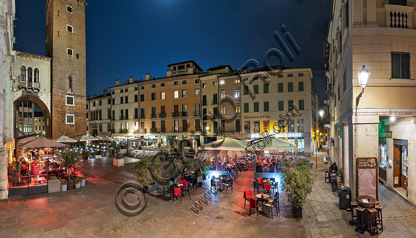 Vicenza, Delle Erbe Square:  night view with bar and restaurant tables. In the background on the left, the medieval Girone Tower, due to the moat that surrounded it, or the Torment Tower, because it was later used as a prison.